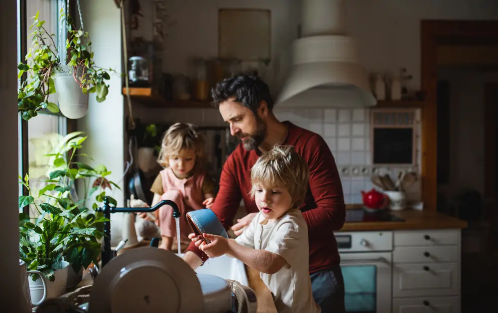 Man doet samen met twee kinderen de afwas in de keuken.