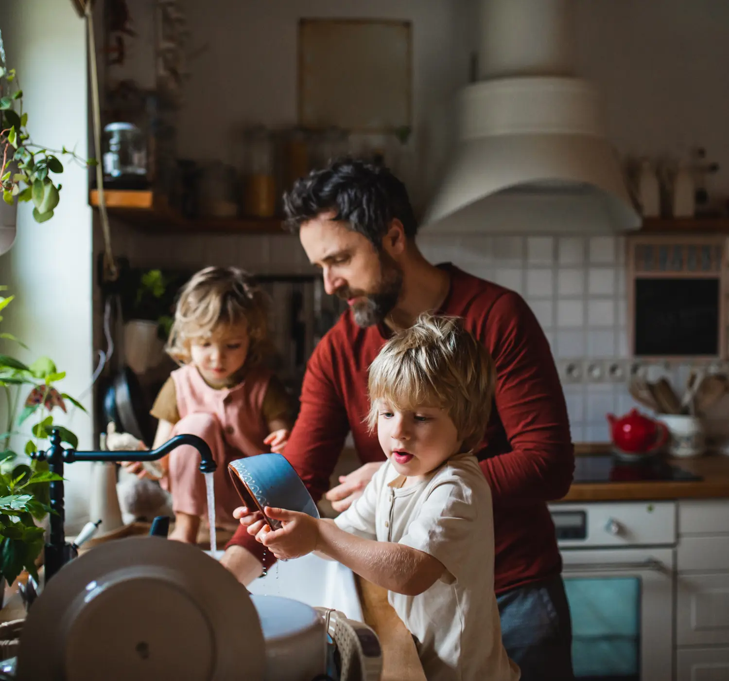 Man doet samen met twee kinderen de afwas in de keuken.