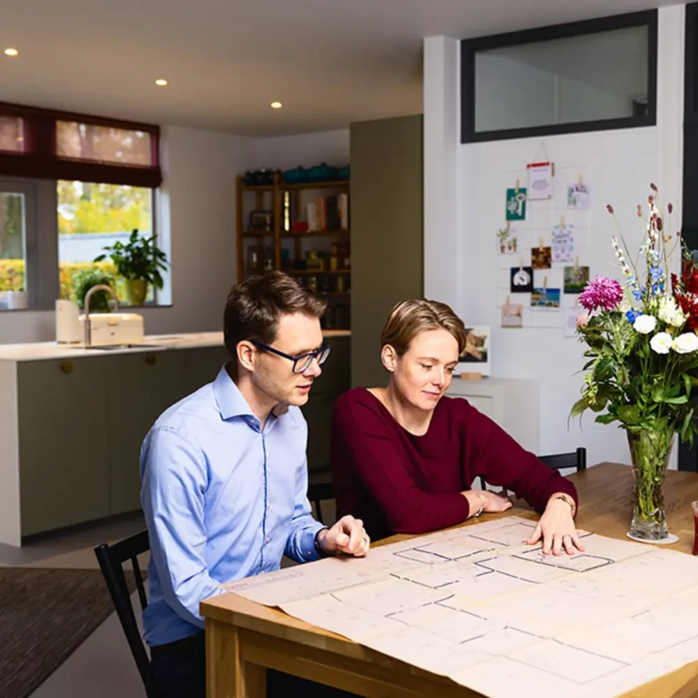 Coralien en haar man zitten aan keukentafel en bekijken bouwtekeningen.